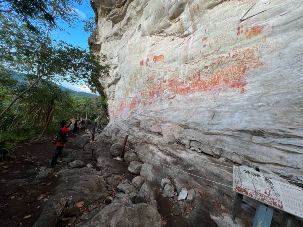 Massive rock art panel at Sierra de La Lindosa with researchers examining ancient paintings beneath the tepui overhang
